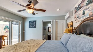 Ein Schlafzimmer mit Bett, Deckenventilator, Kunstwerken und Blick ins Freie.