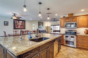 A kitchen with granite countertops, stainless steel appliances, wooden cabinets, and pendant lighting.