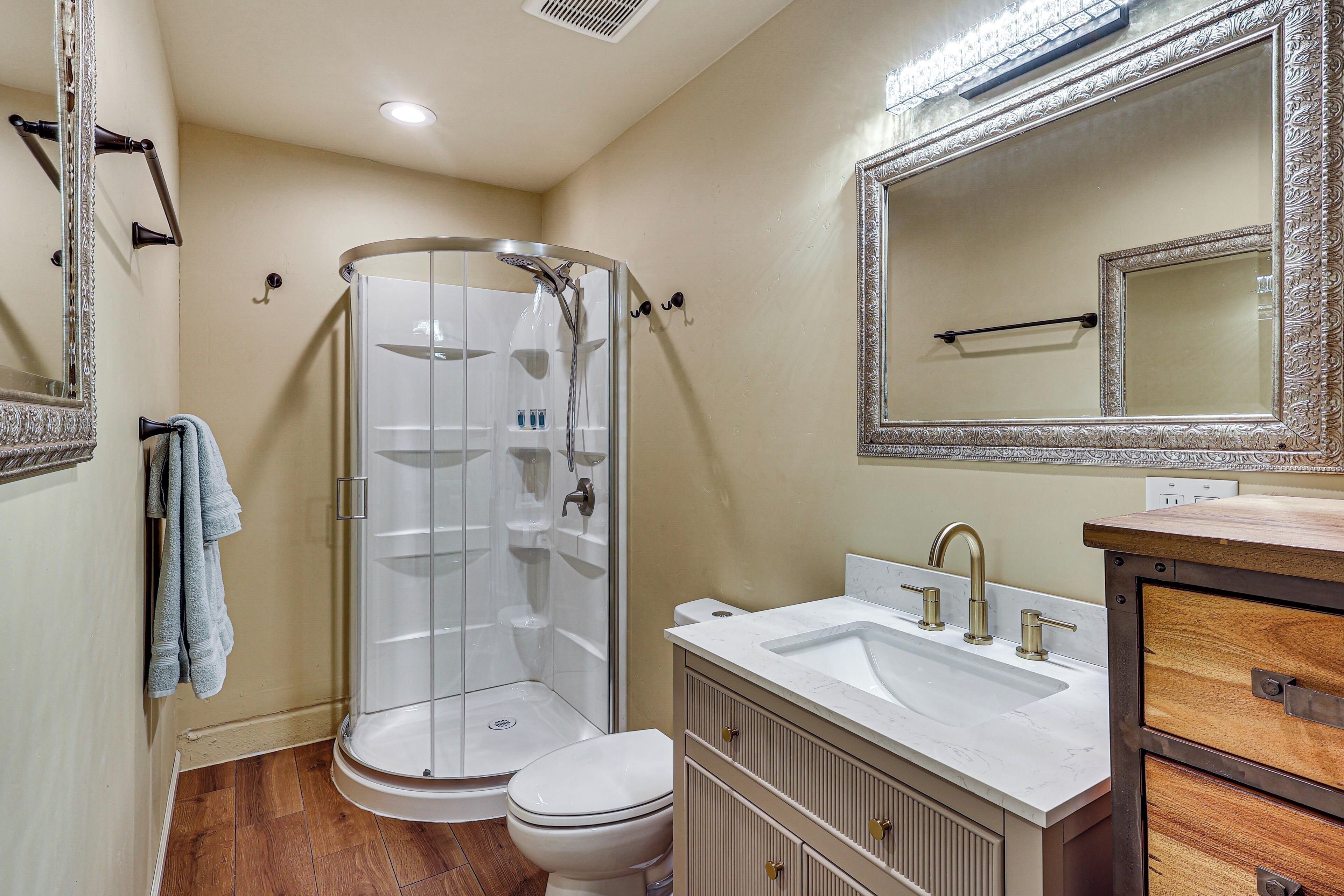 A bathroom with a glass shower enclosure, a white toilet, a sink with a vanity, and a large mirror.