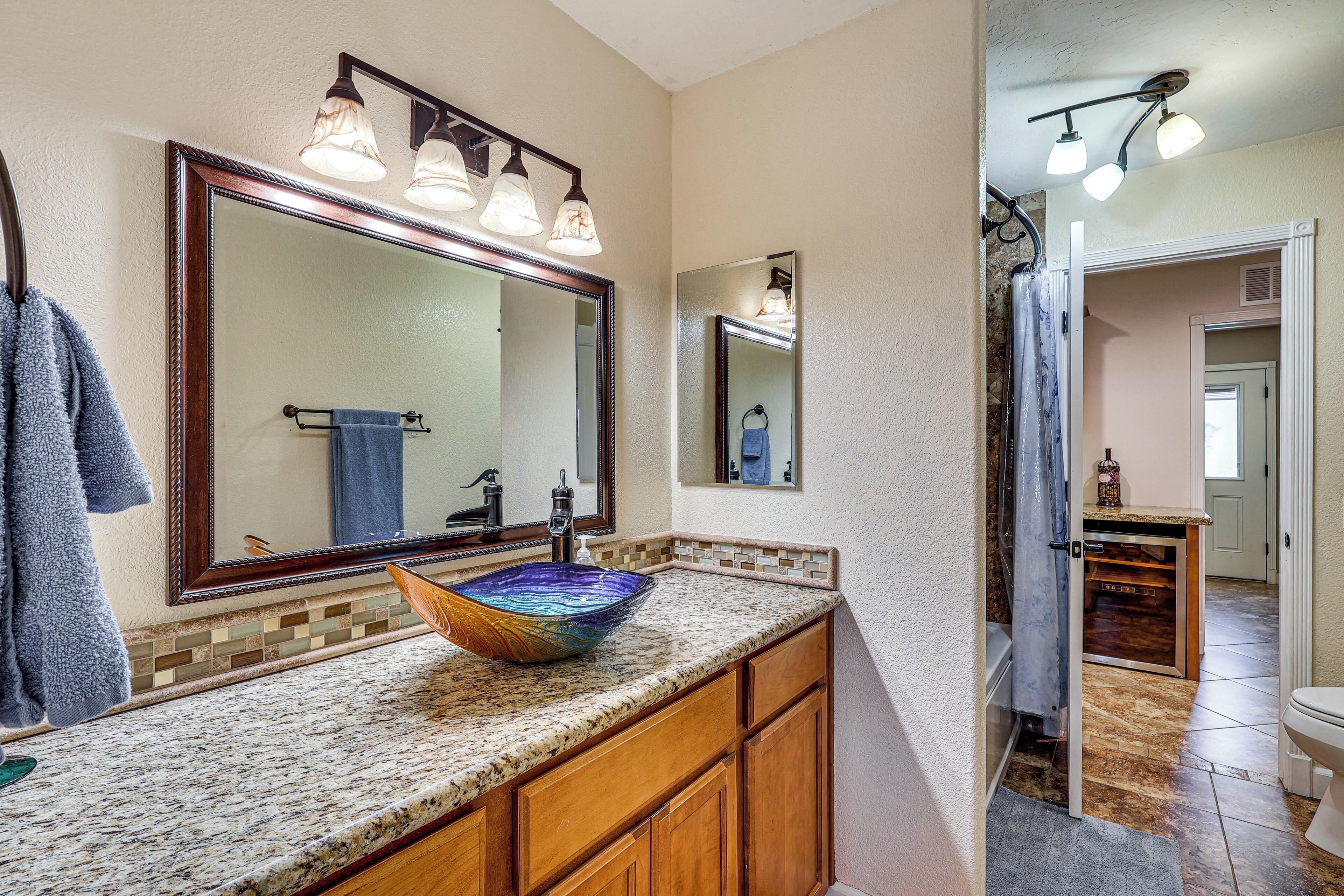 A bathroom with a large mirror, a vessel sink, wooden cabinets, and a shower area.
