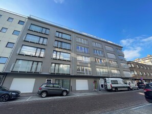 Ein mehrgeschossiges Wohngebäude mit Balkonen, einer Garage und geparkten Autos.