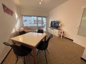 Ein Wohnzimmer mit Esstisch, Stühlen, einer Couch, einem Fernseher und einem kleinen Tisch mit Lampen.