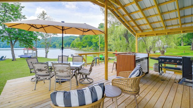A covered deck with outdoor furniture, a grill, and a view of a lake. - Lakefront Home and 2 Cabins on Claytor Lake (Hiwassee)