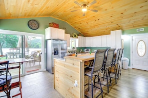 A kitchen with wooden cabinets, a central island with chairs, a refrigerator, and a ceiling fan. - Private Beach! Home w/ 2 Guest Cabins in Hiwassee (Hiwassee)