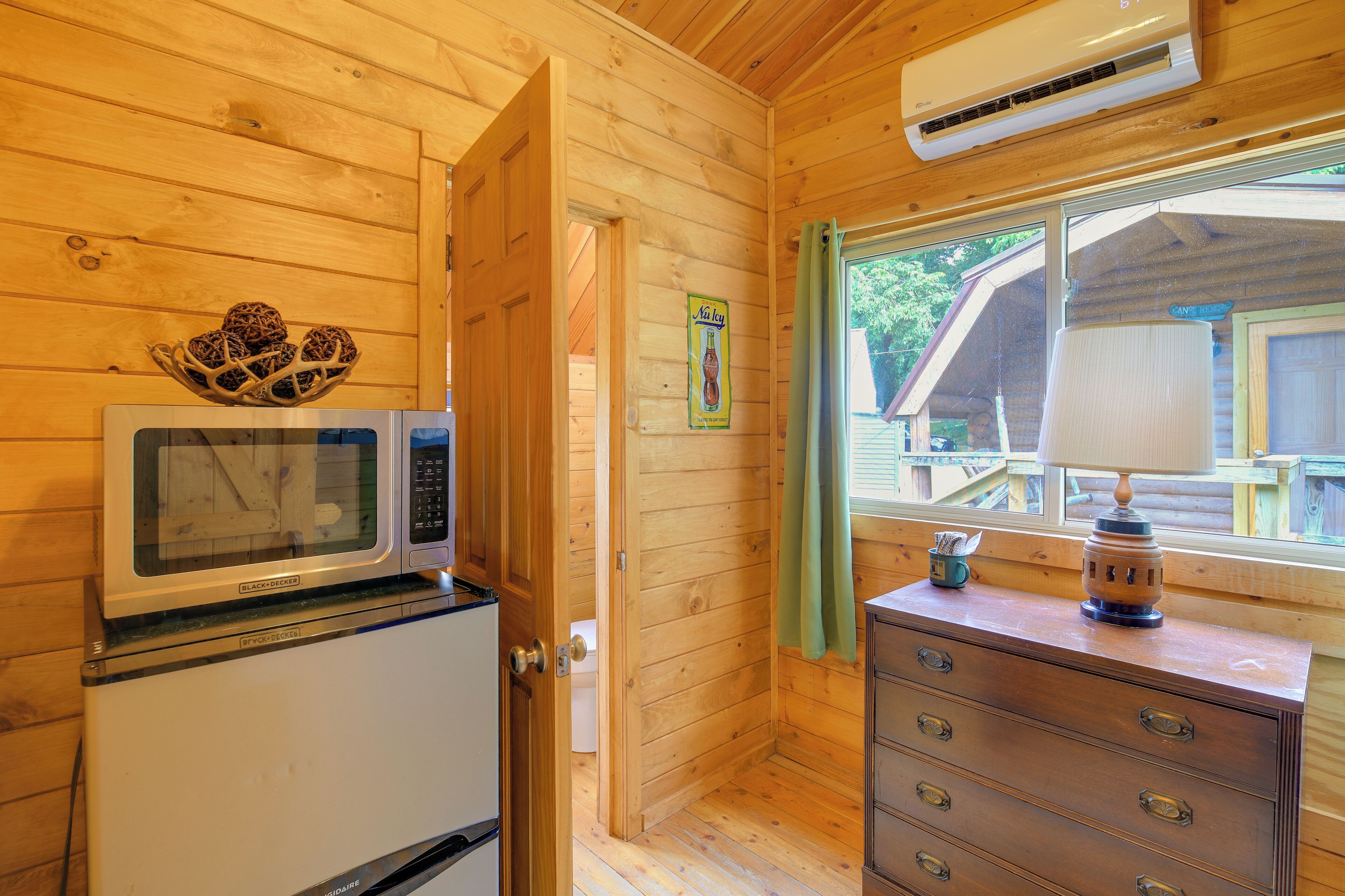 Ein Holzhütten-Interieur mit Mikrowelle, kleinem Kühlschrank, Holzkommode und Fenster mit Blick hinaus.