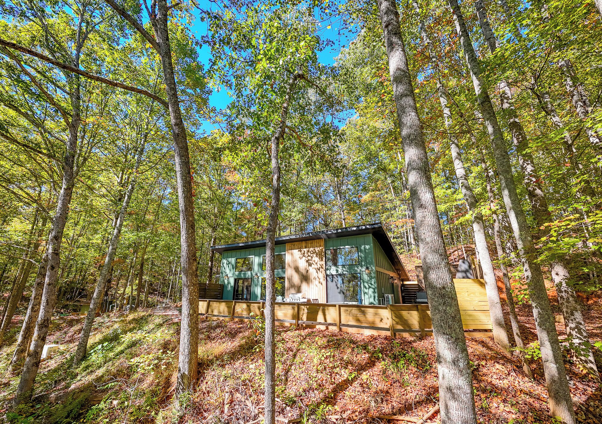 Una cabaña en un bosque con terraza de madera y un ventanal grande.