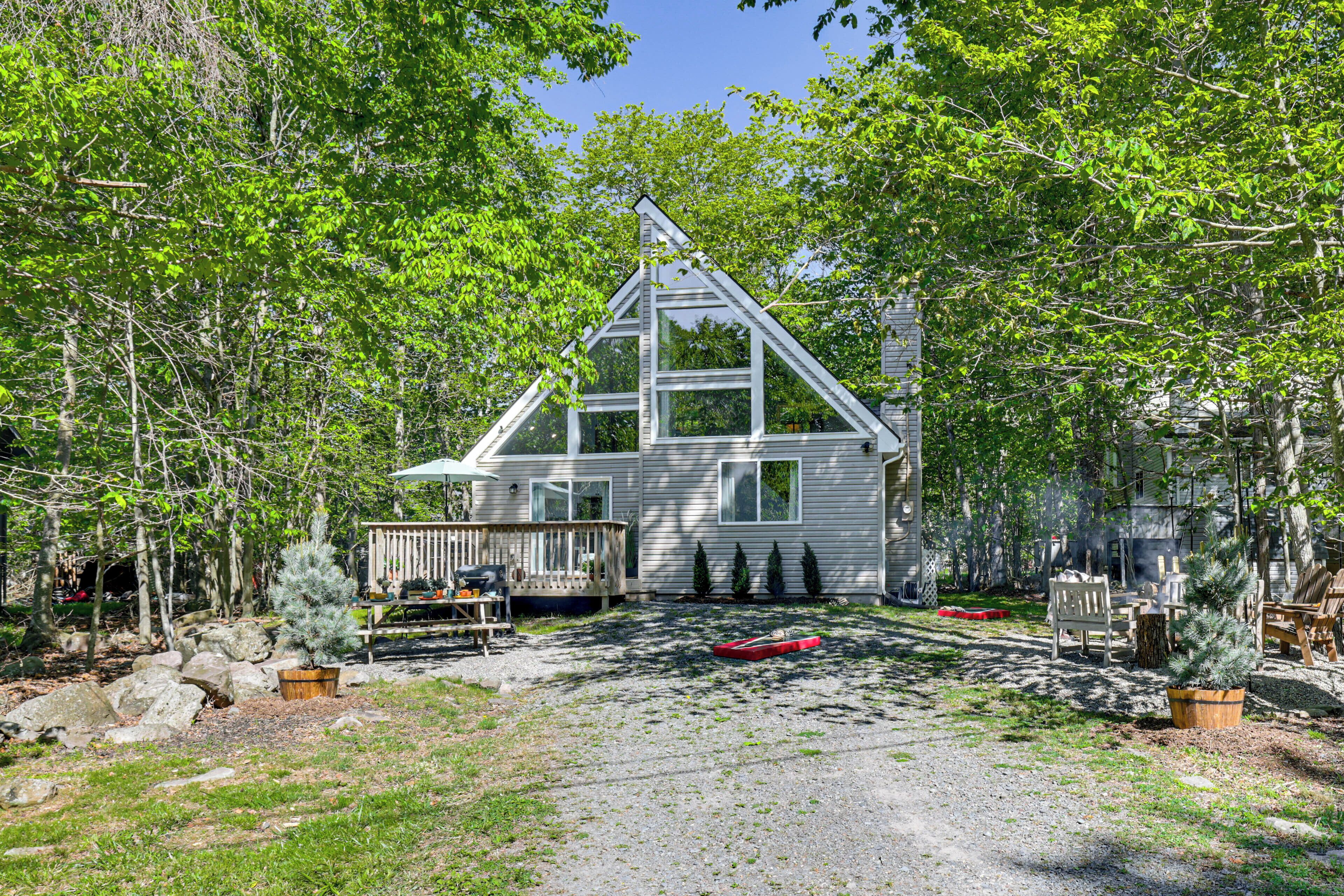 A house with a triangular roof, surrounded by trees and a gravel path.