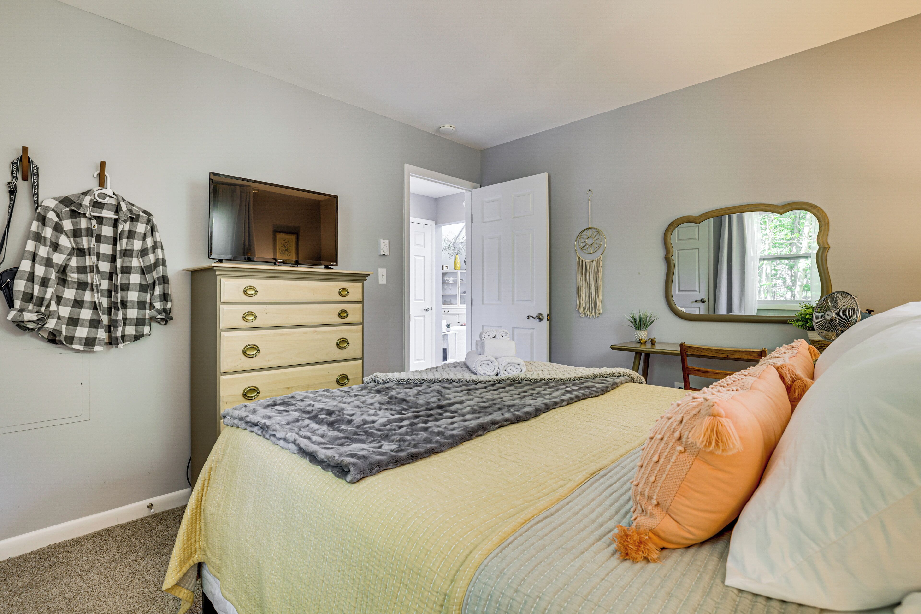 Ein Schlafzimmer mit Bett, Kommode, Spiegel und einer Tür zu einem anderen Raum.