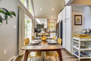 Une cuisine moderne avec des meubles blancs, une table à manger pour six personnes et un îlot de cuisine équipé d’un four à micro-ondes.