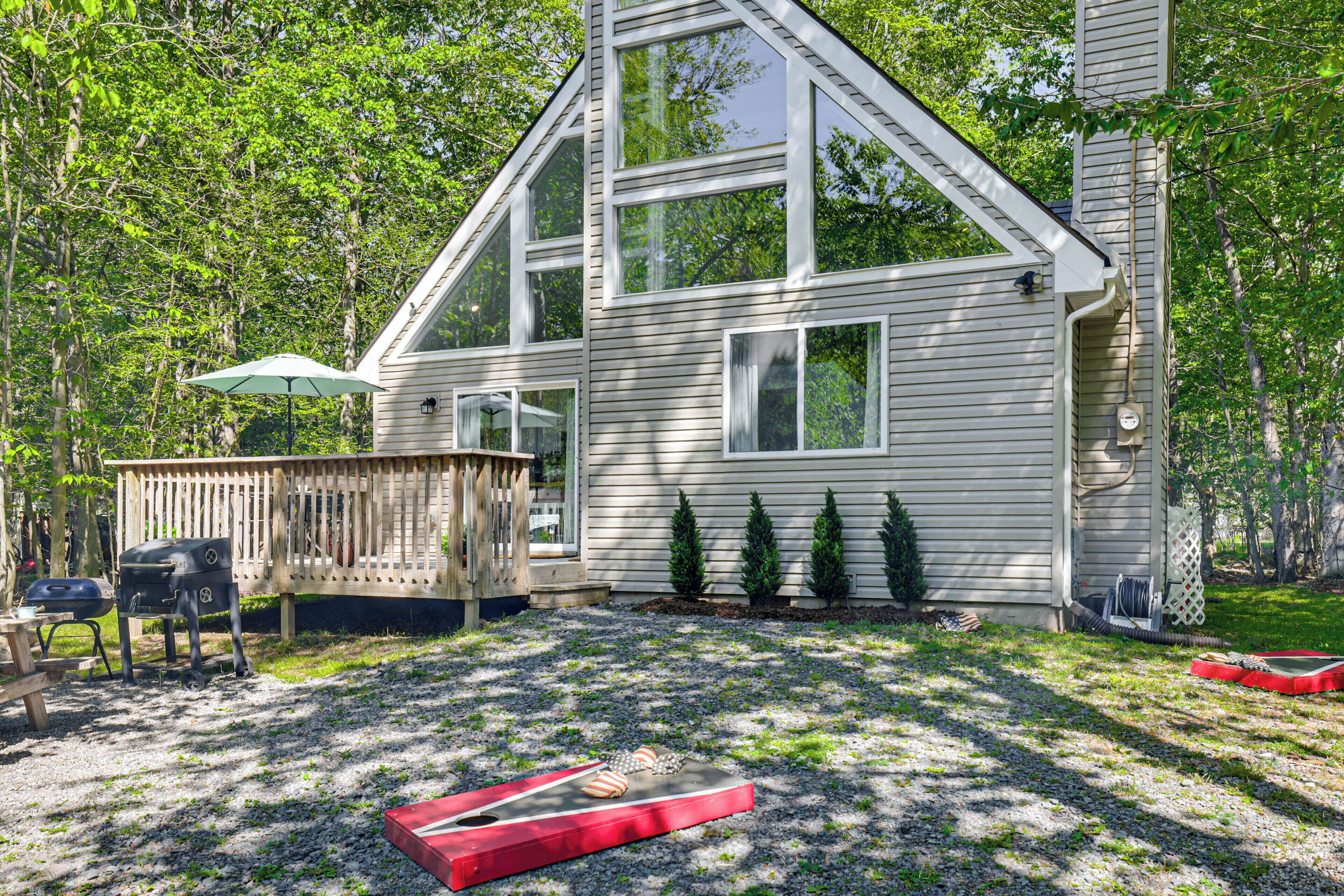 A house with a sloped roof, a deck, a grill, and a trampoline.