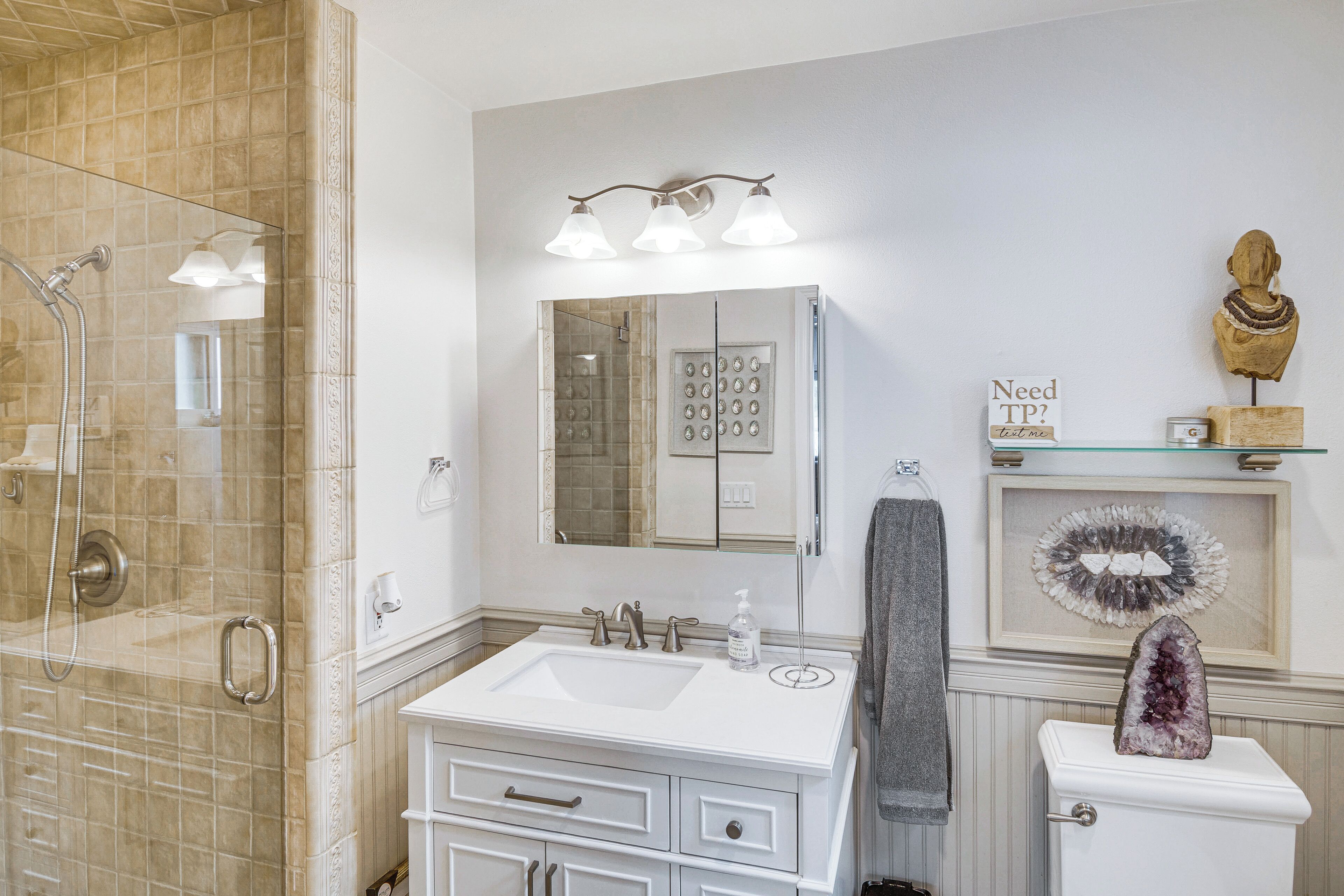 A bathroom with a glass shower enclosure, a white sink with a mirror above, and a toilet with a decorative stone.