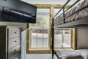 A bunk bed room with a TV mounted above the bed, a dresser, and a window with a view of the outside.
