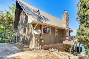 A two-story house with a stone chimney, satellite dish, and a balcony overlooking a body of water.
