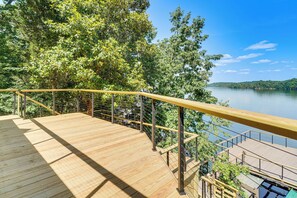A wooden deck with a metal railing overlooking a lake, surrounded by trees.