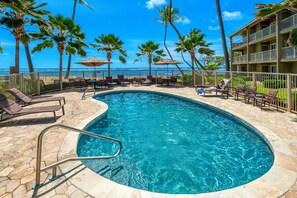 A pool area with lounge chairs and umbrellas, surrounded by palm trees and a view of the ocean. - Beachfront with air conditioning, great walkable and central Kapaa location (Kapaa)