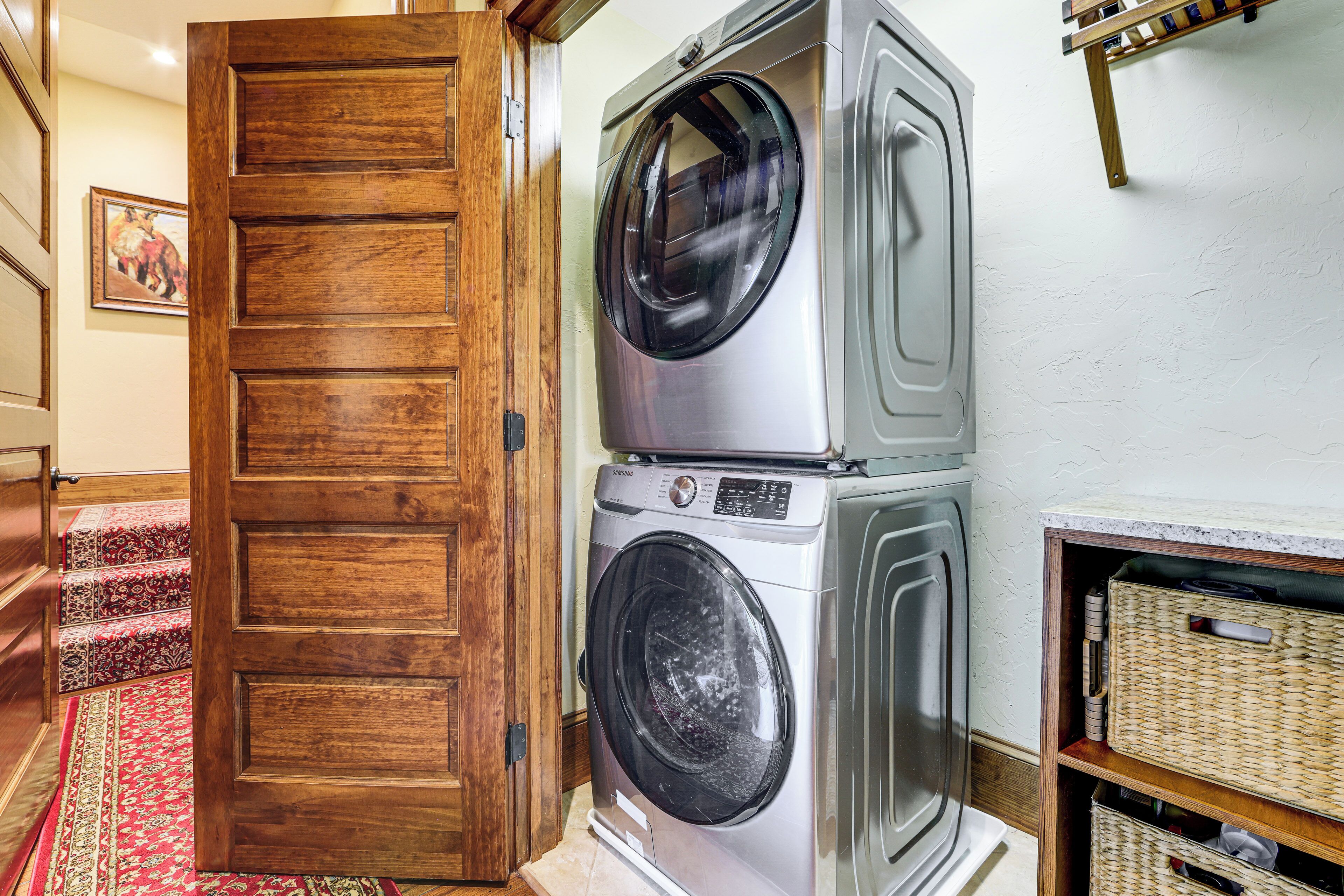 A laundry area with stacked washers and dryers, a wooden door, and a carpeted staircase.