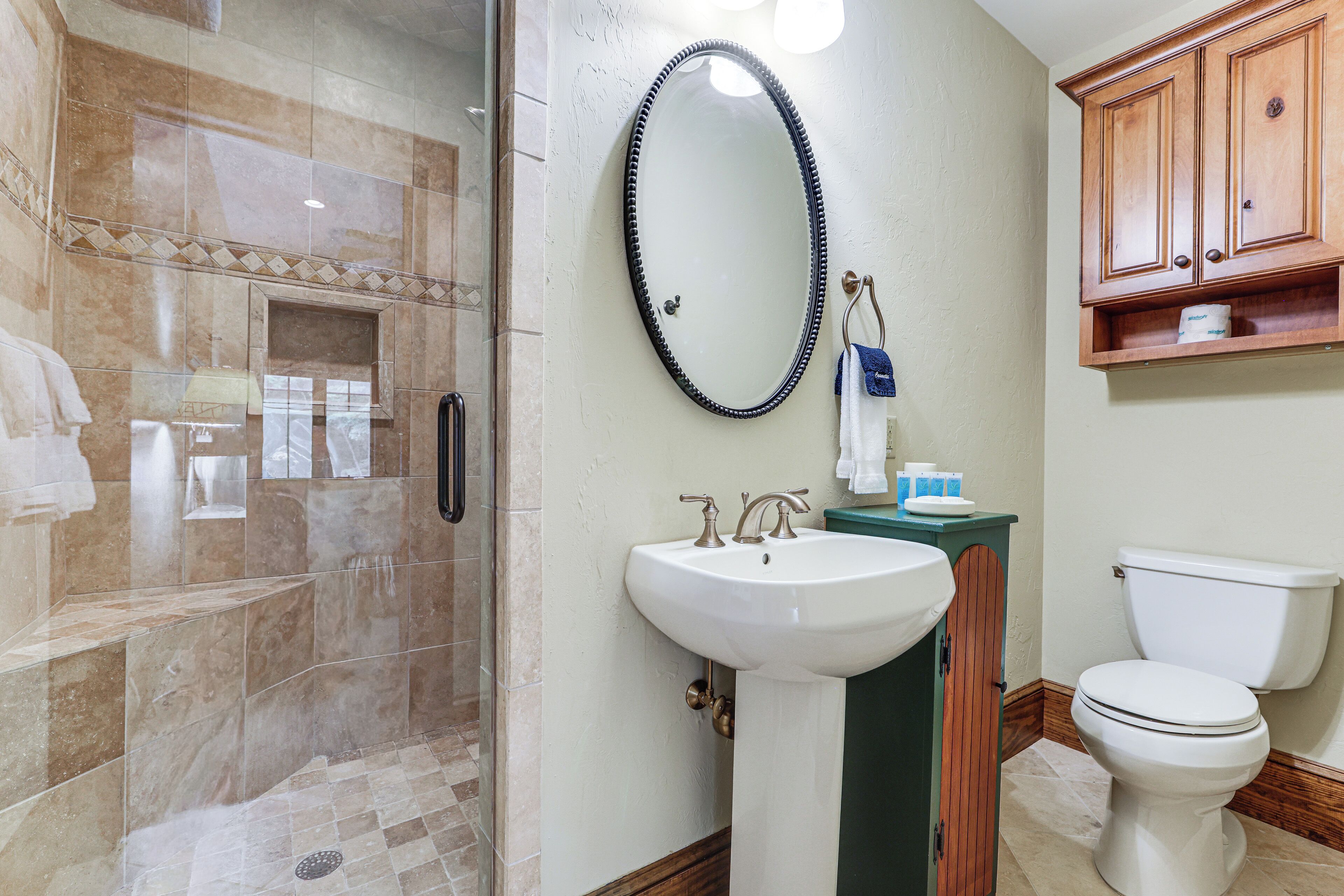 A bathroom with a shower, sink, toilet, and wooden cabinets.