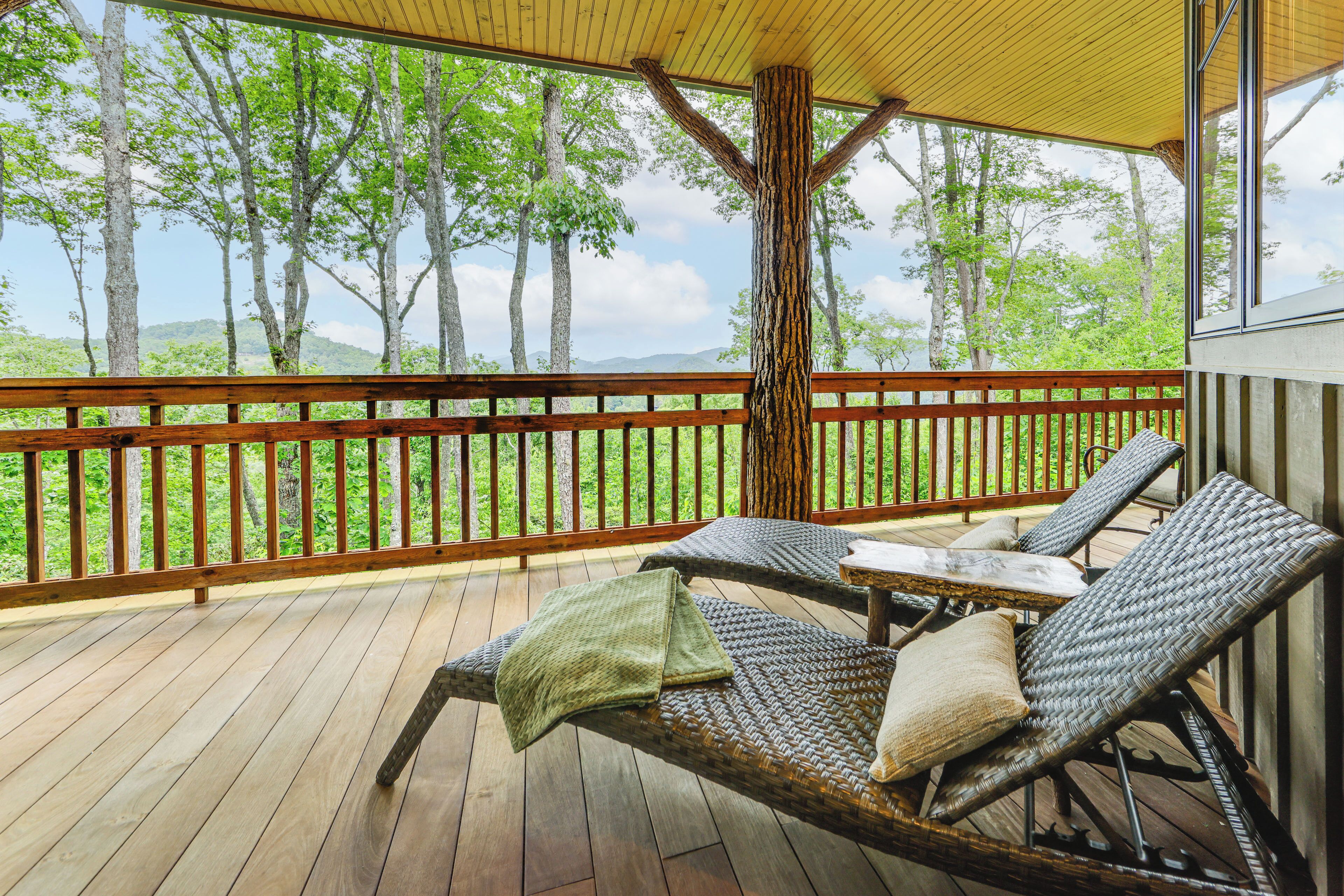 Une terrasse en bois avec des fauteuils de jardin en osier et une table, donnant sur une zone boisée.