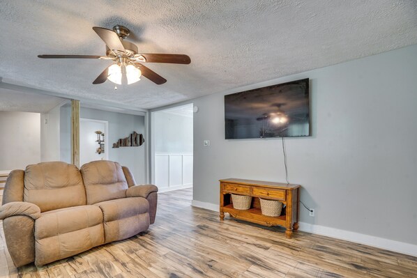 A living room with a ceiling fan, a sofa, a wooden console table, and a painting on the wall. - Family-friendly Home Near Kentucky Lake! (Dexter)