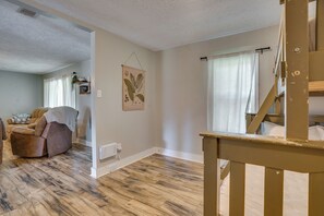 Quarto com piso de madeira, uma cadeira de couro marrom, um radiador branco e uma janela com cortinas.