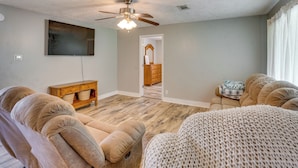 A living room with a ceiling fan, a flat-screen TV, a wooden cabinet, and a beige sofa. - Family-friendly Home Near Kentucky Lake! (Dexter)