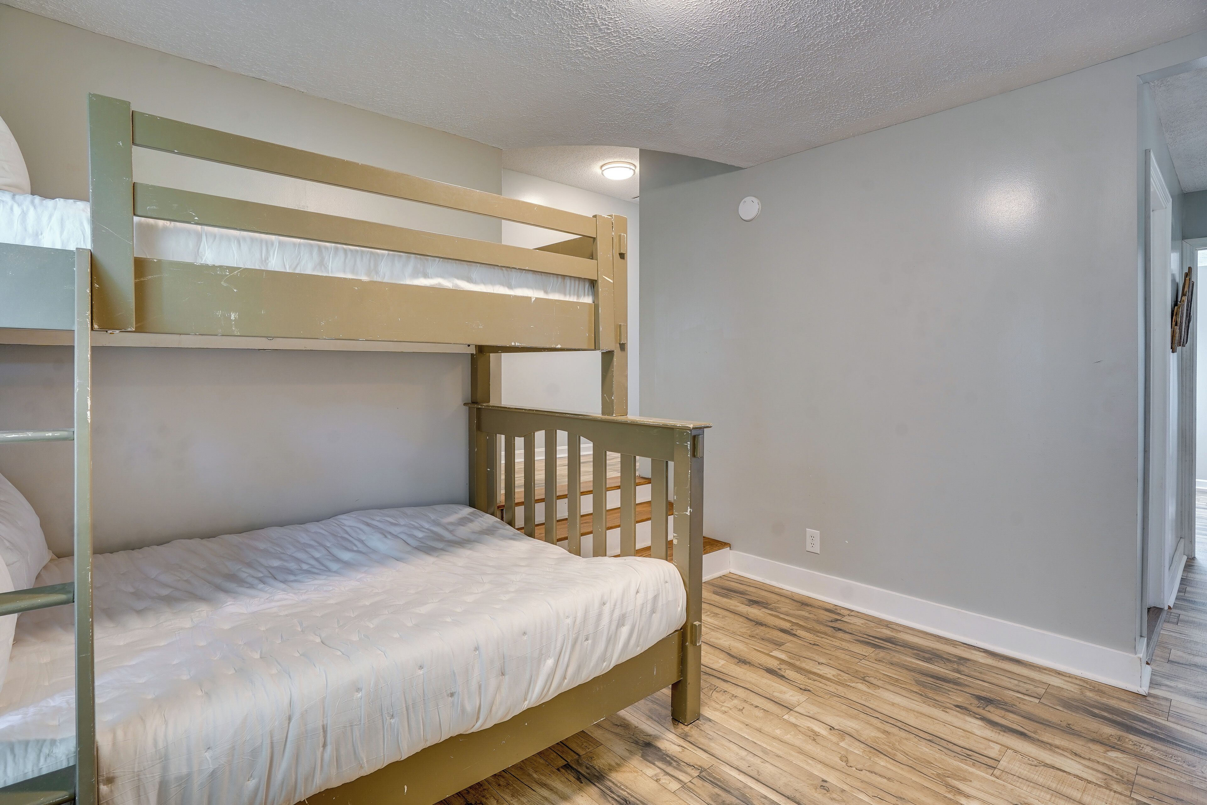 A bunk bed room with a wooden frame, a white mattress, and a wooden floor.