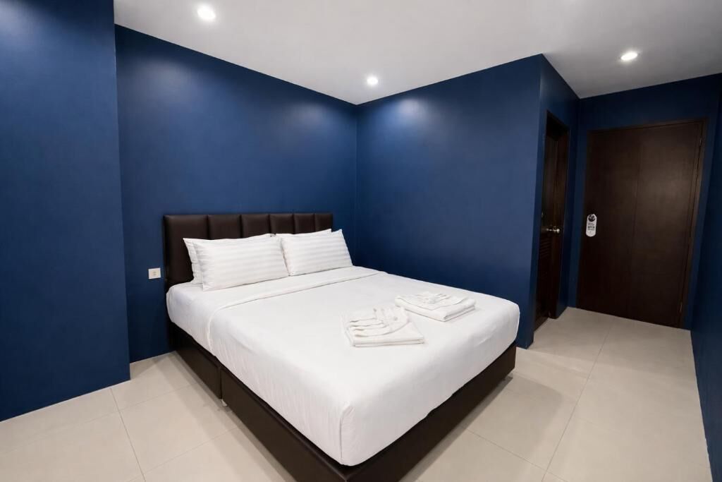 A bedroom with a large bed, dark headboard, white bedding, and blue walls.