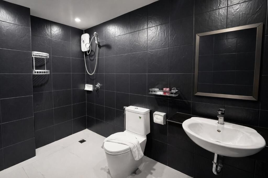 A modern bathroom with black tiles, a white toilet, a sink, and a shower.
