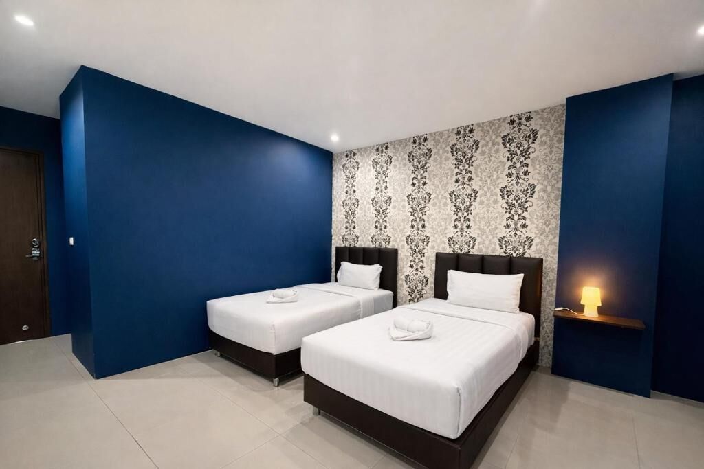 A hotel room with two beds, a patterned wallpaper, and a nightstand with a lamp.