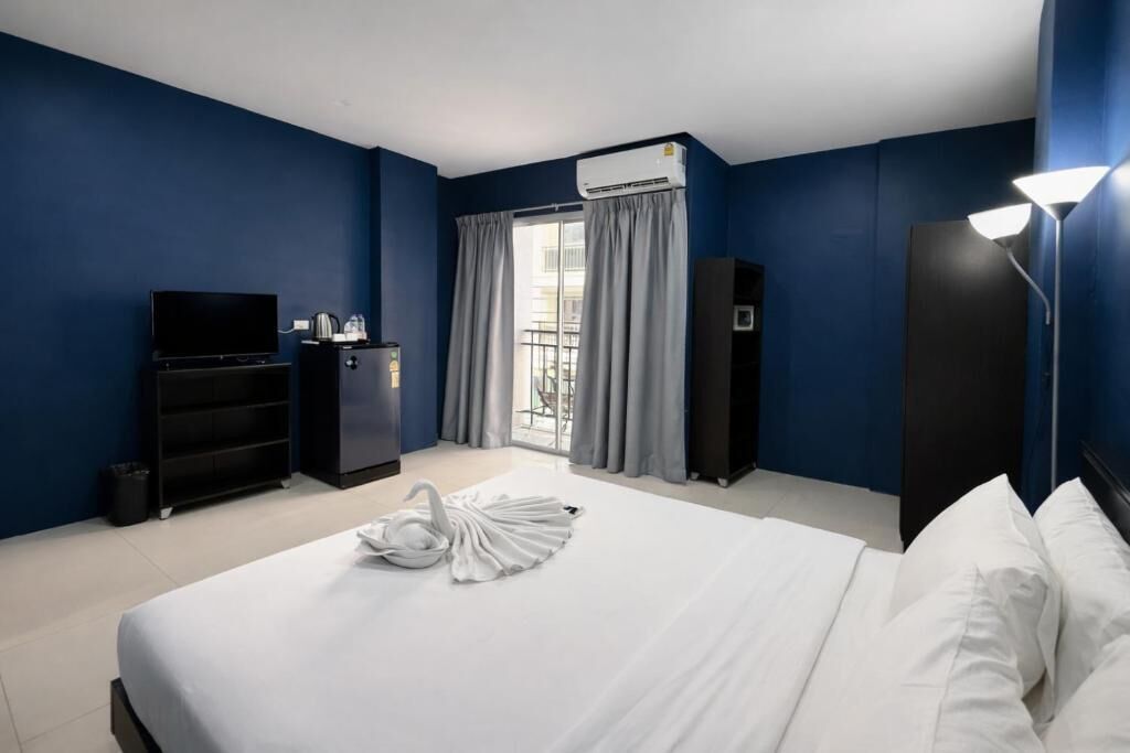 A hotel room with a bed, a TV, a minibar, a wardrobe, and a balcony with curtains.
