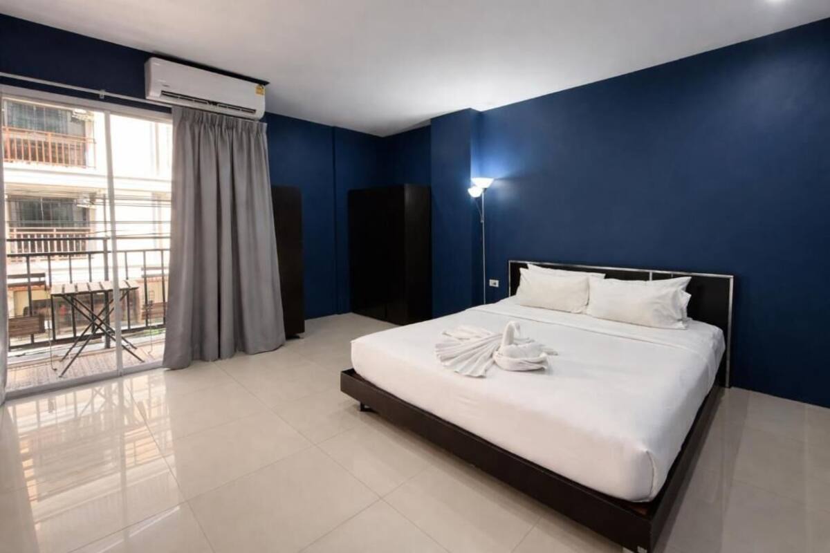A hotel room with a bed, a balcony with a view, a standing lamp, and an air conditioning unit.