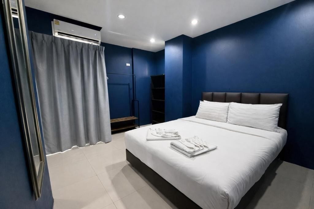 A hotel room with a bed, white linens, a grey curtain, an air conditioning unit, and a built-in wardrobe.