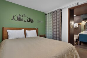 A hotel room with a bed, a green wall with a mountain design, a bathroom with a blue sink, and a curtain with a circular pattern. - Newly renovated 1 bedroom, ground floor, extra amenities (Winter Park)