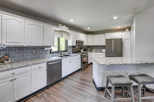 A modern kitchen with white cabinetry, granite countertops, stainless steel appliances, and a central island with bar stools.