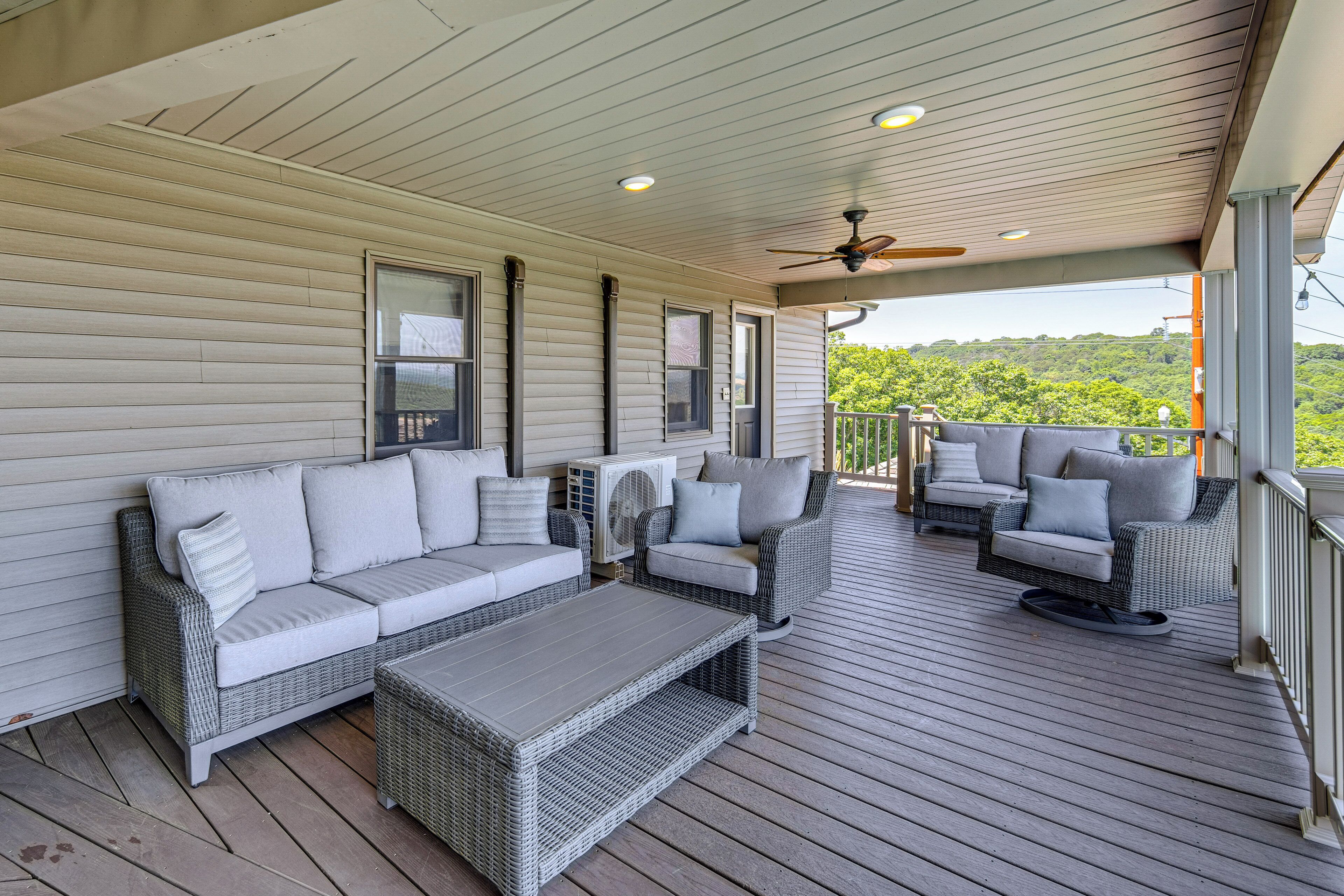 A covered porch with wicker furniture, a ceiling fan, and a view of greenery.