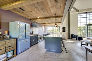 Una cocina moderna con una isla central, vigas de madera en el techo y grandes ventanales.