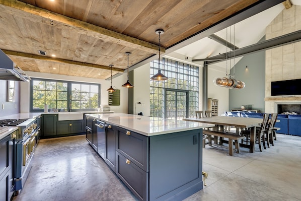 A modern kitchen with a large island, wooden ceiling beams, and pendant lighting.