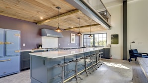 Een moderne keuken met een groot eiland, barstoelen en een trap naar een verdieping erboven.