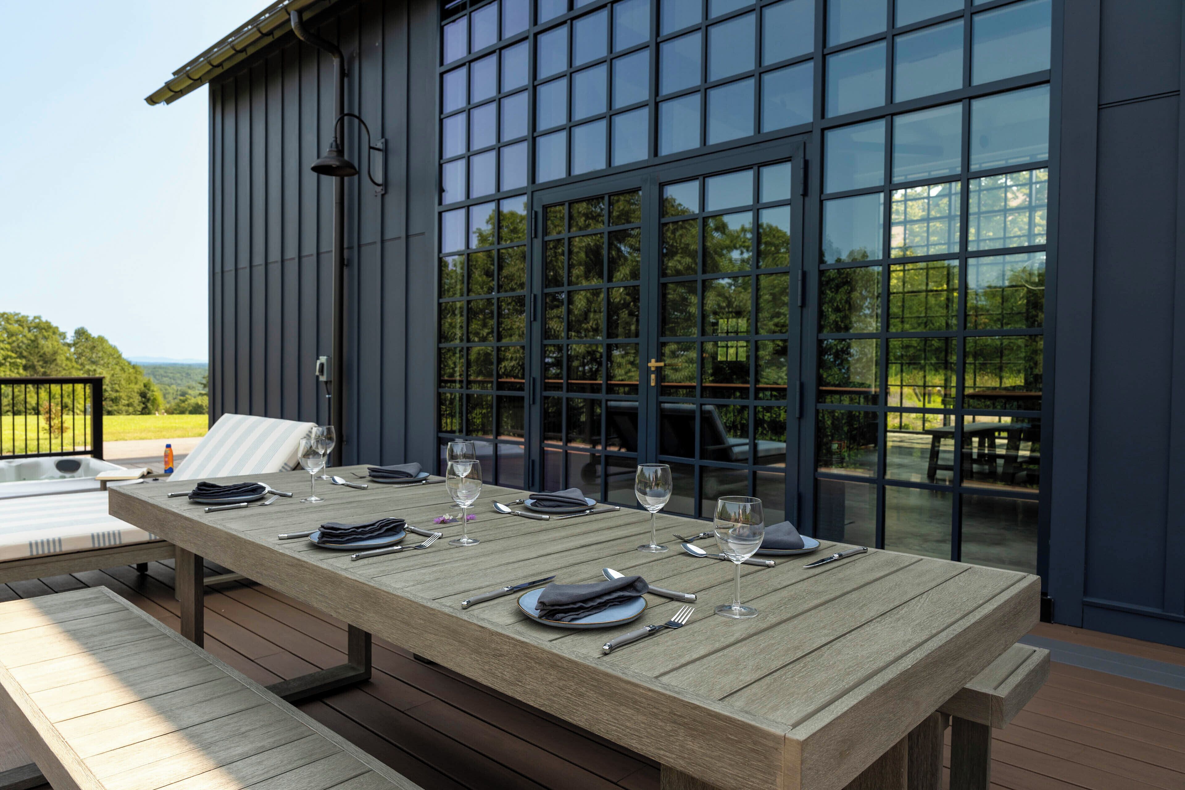 An outdoor dining area with a table set for two, a hot tub, and a view of a modern building with large windows.