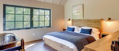 A bedroom with a large window, a wooden bed, a nightstand, a headboard, and a wooden desk with a chair.