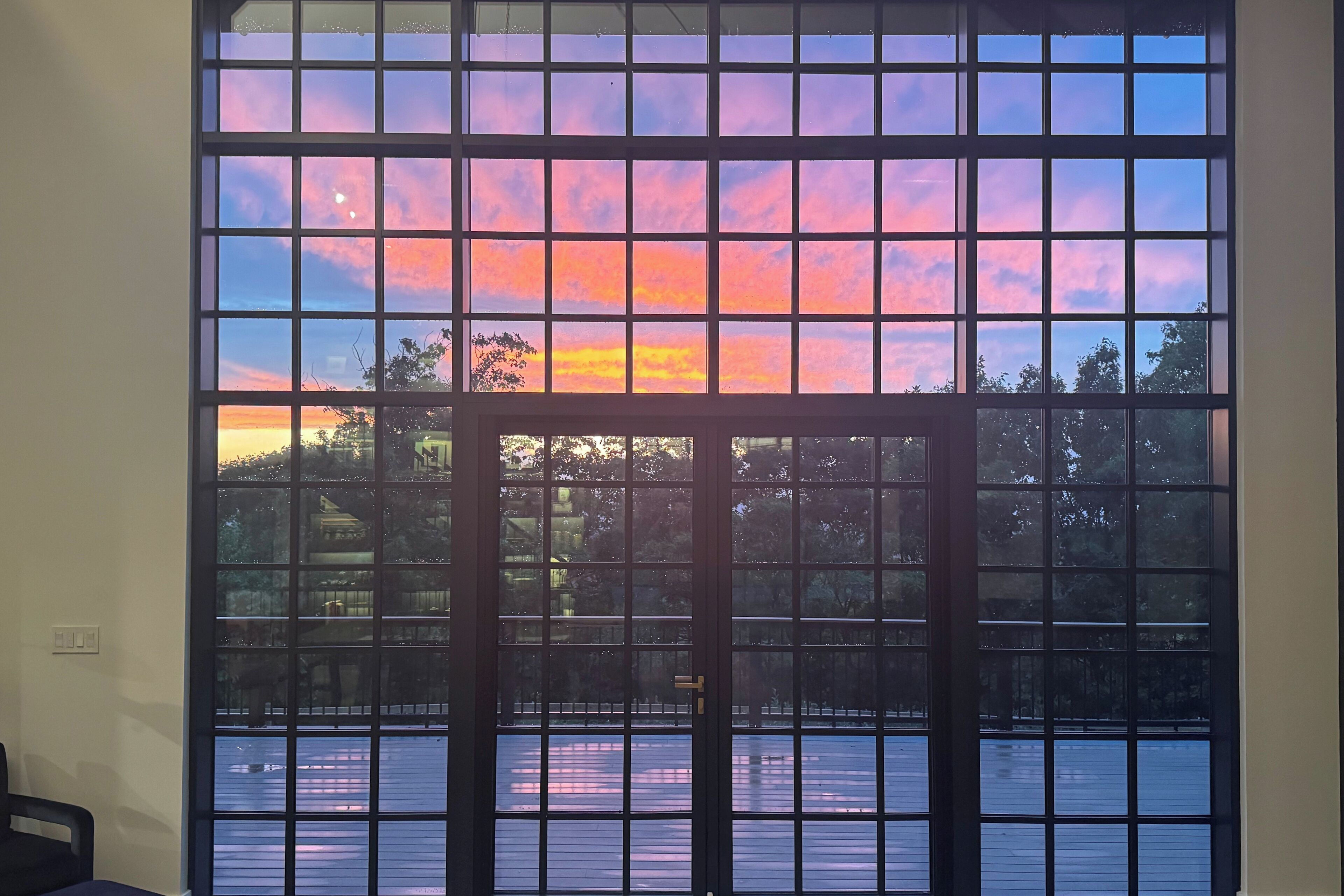 A room with a large window featuring a grid pattern, a door, and a view of a body of water and trees.