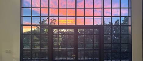 A room with a large window featuring a grid pattern, a door, and a view of a body of water and trees.