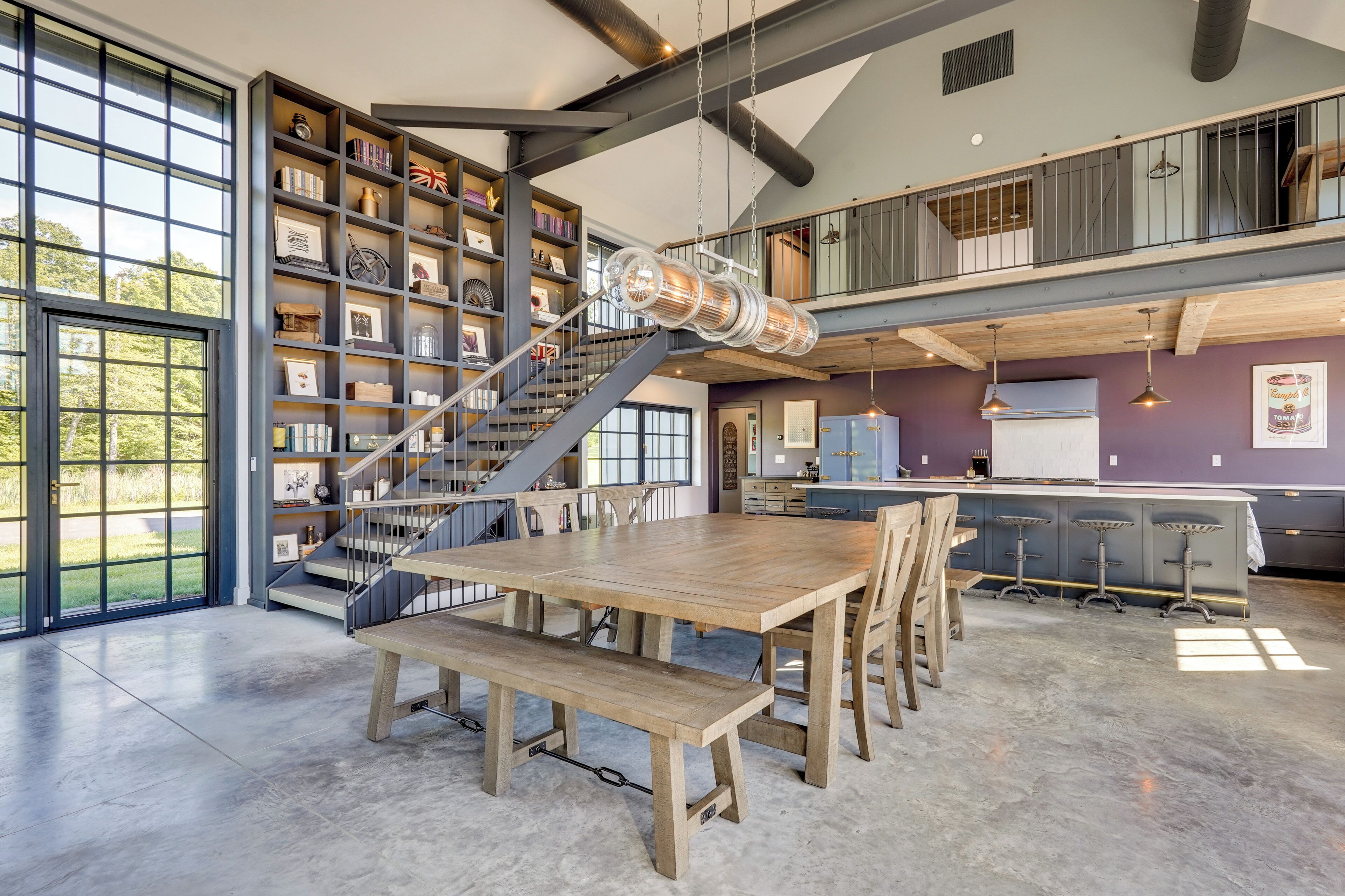 Una habitación amplia con una gran mesa de madera, una escalera y una estantería llena de libros y adornos.