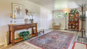 A room with a large patterned rug, a wooden console table with drawers, a wicker chair, a bookshelf, and a window with a view of greenery. - Walk to Shops & Eats! Family Escape in Columbus (Columbus)