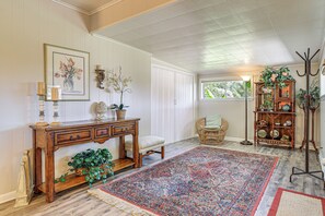 A room with a large patterned rug, a wooden console table with drawers, a wicker chair, a bookshelf, and a window with a view of greenery. - Walk to Shops & Eats! Family Escape in Columbus (Columbus)