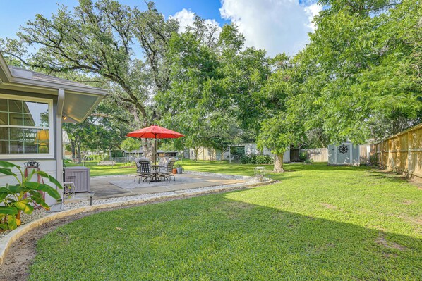 A backyard with a patio, outdoor furniture, and a red umbrella.
