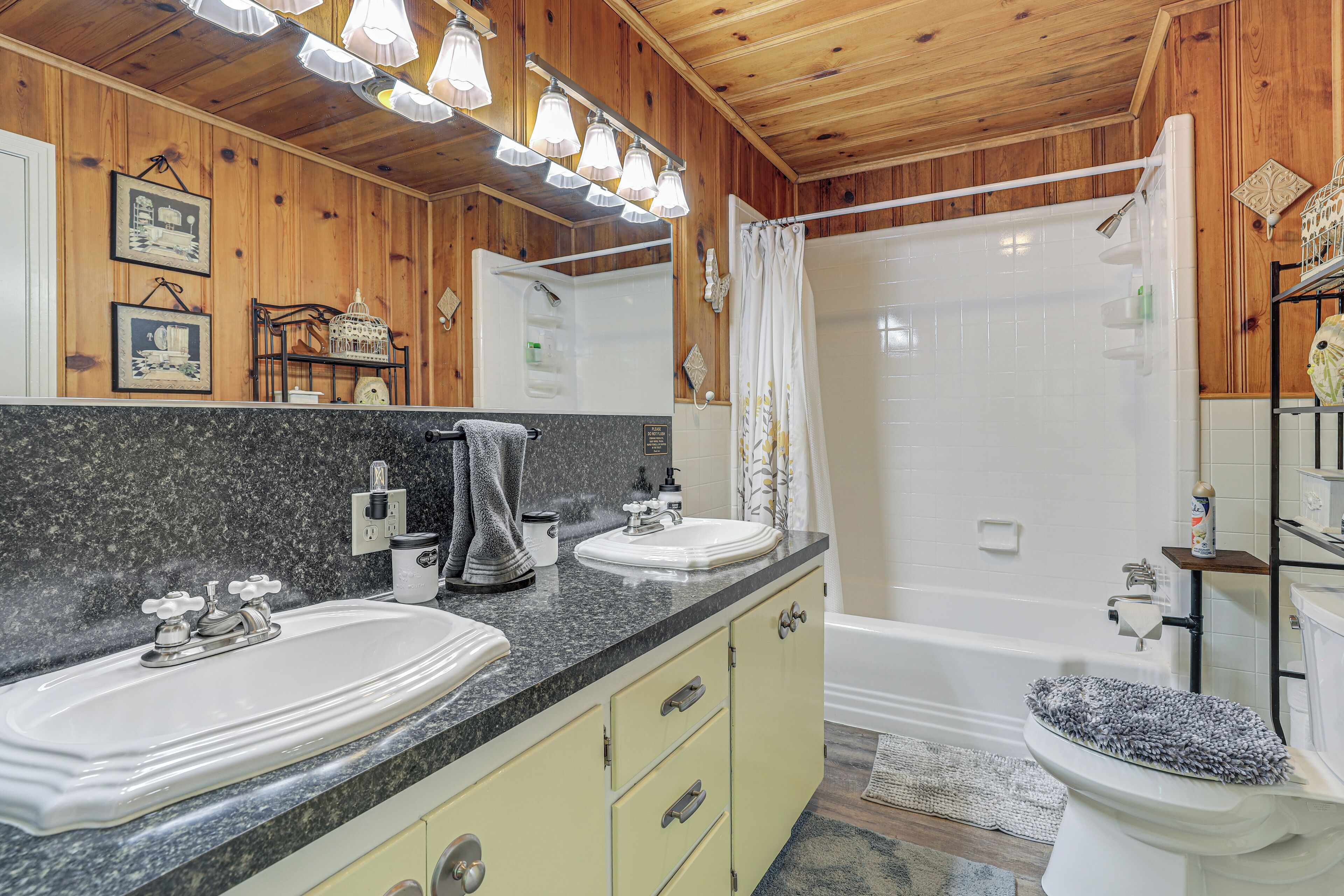 Une salle de bain avec des lambris en bois, un meuble-lavabo à deux vasques, une baignoire et un rideau de douche.