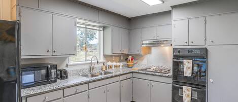 Una cocina moderna con armarios grises, un refrigerador de acero inoxidable, un microondas, un fregadero y un horno empotrado.