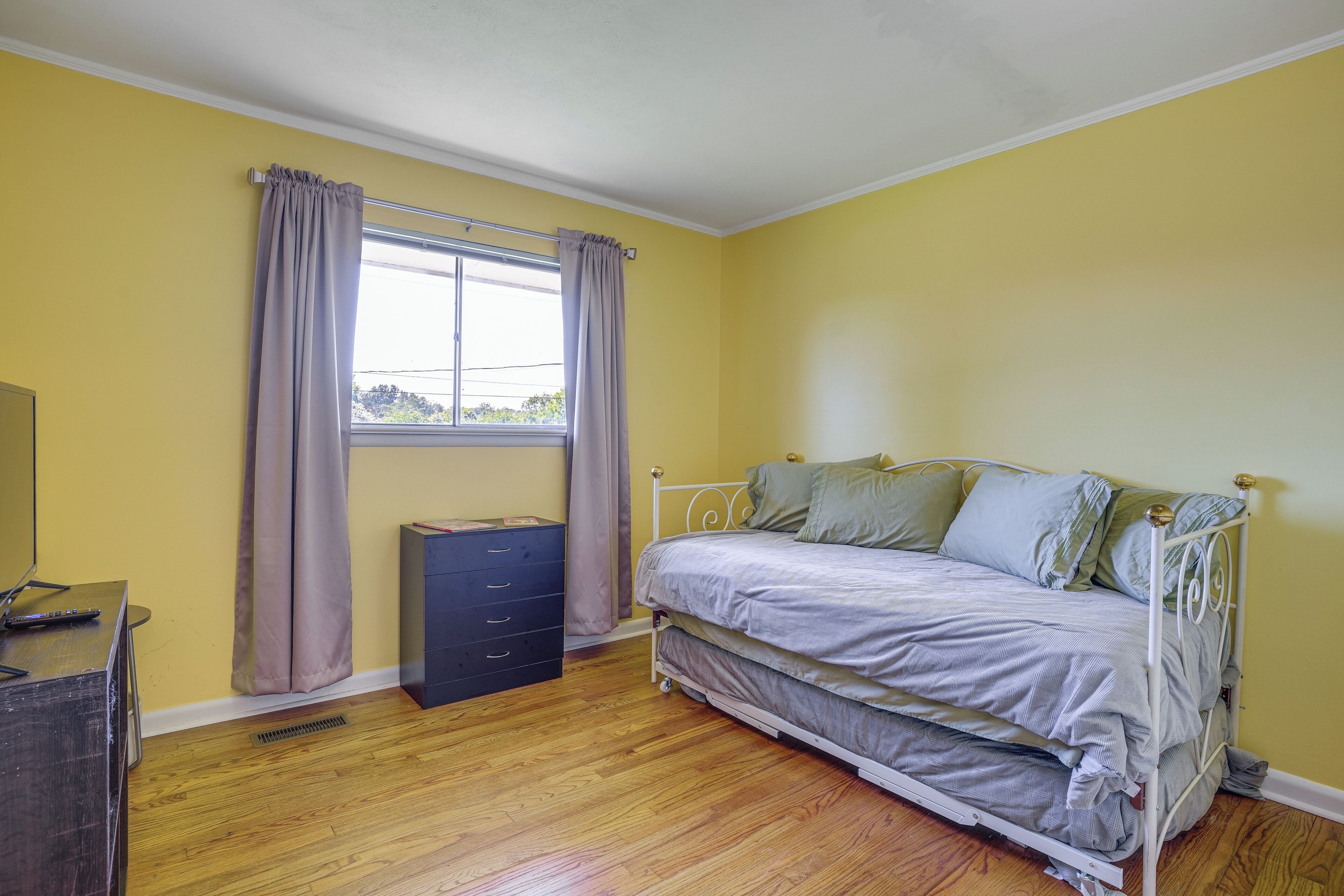Une chambre à coucher avec un lit, une commode, une fenêtre avec des rideaux et un radiateur.