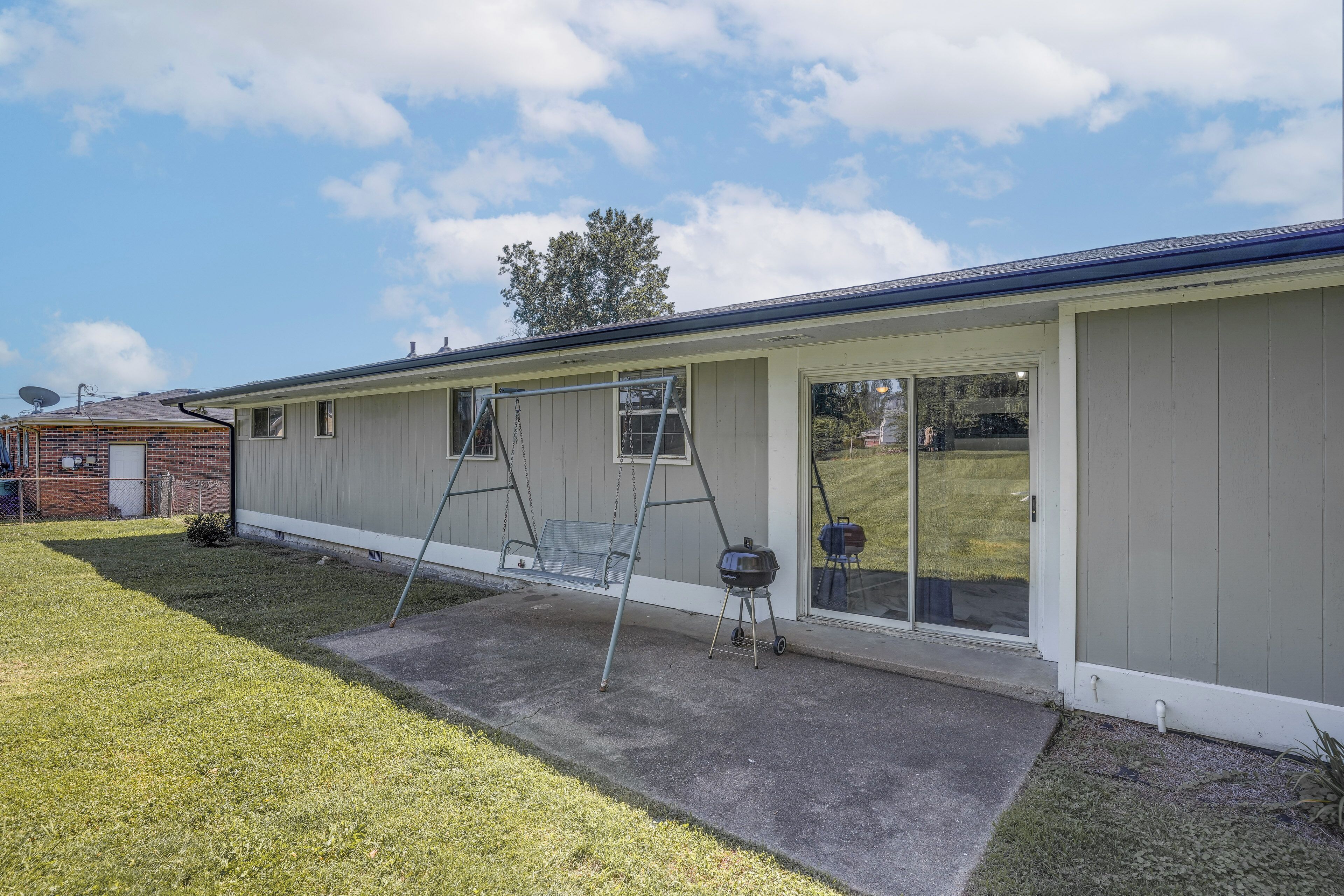 A single-story building with a covered patio, a swing set, and a barbecue grill.